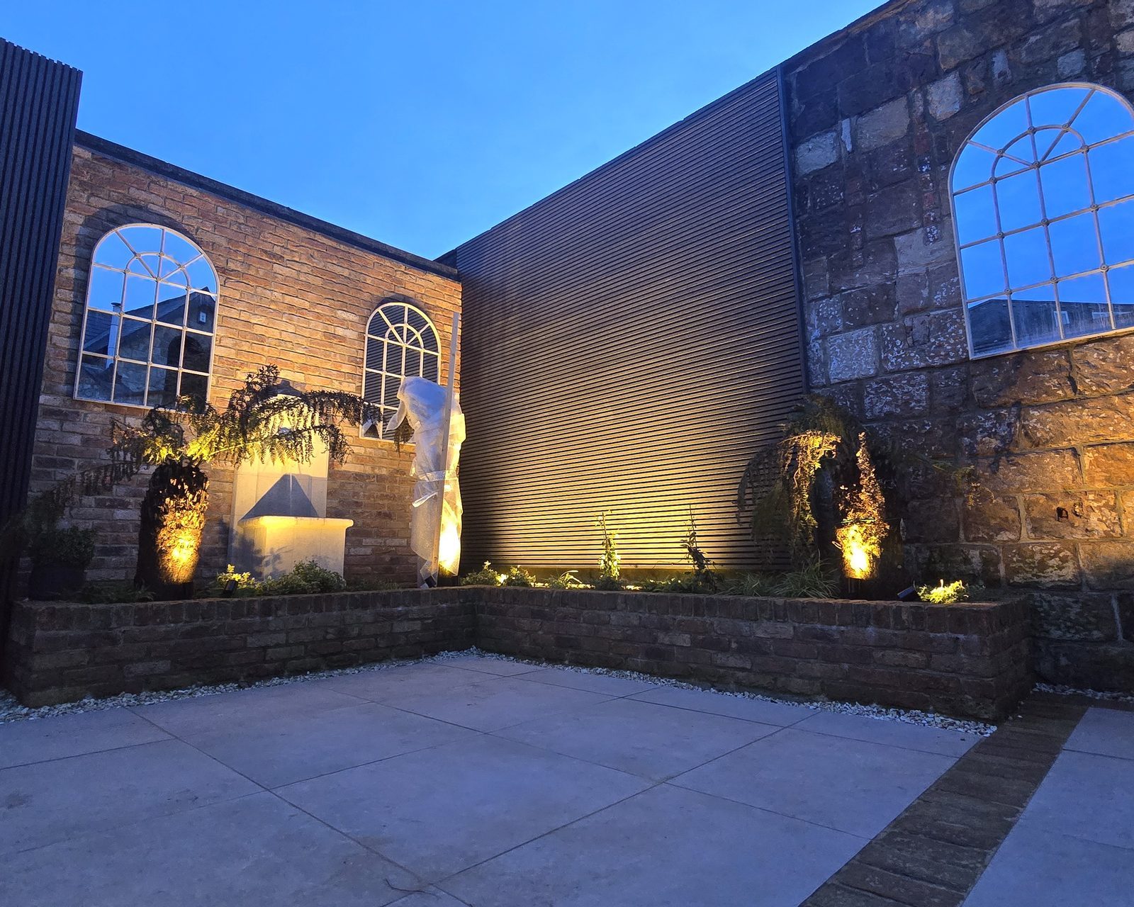 Courtyard garden at dusk lit by wall uplights and spike lights